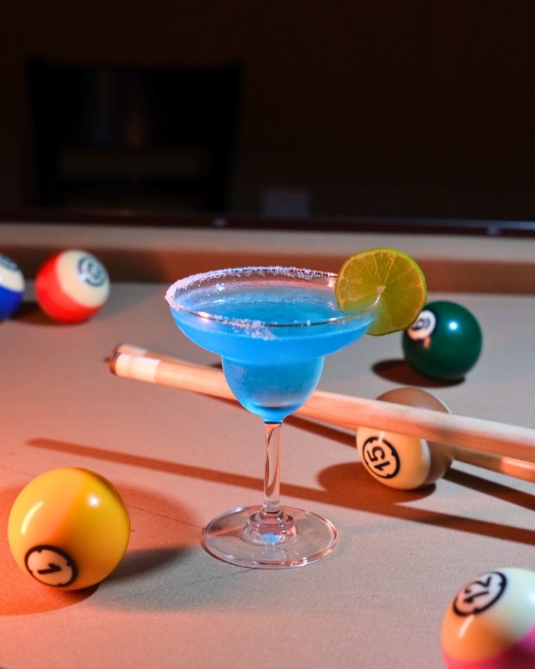 Blue cocktail drink on table with pool balls and cue stick